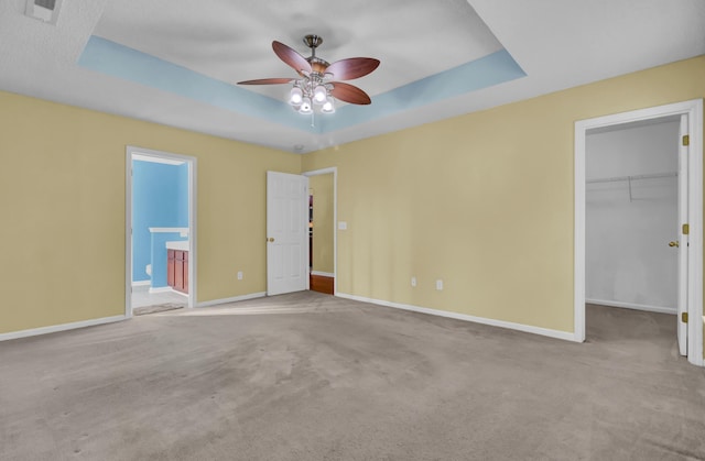 unfurnished bedroom featuring ensuite bathroom, a walk in closet, light colored carpet, a tray ceiling, and a closet