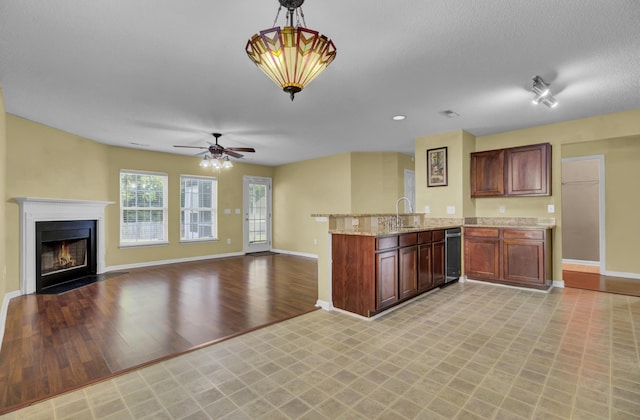 kitchen featuring light stone counters, decorative light fixtures, kitchen peninsula, ceiling fan, and light hardwood / wood-style floors