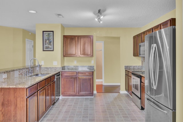 kitchen with sink, appliances with stainless steel finishes, light stone countertops, a textured ceiling, and kitchen peninsula