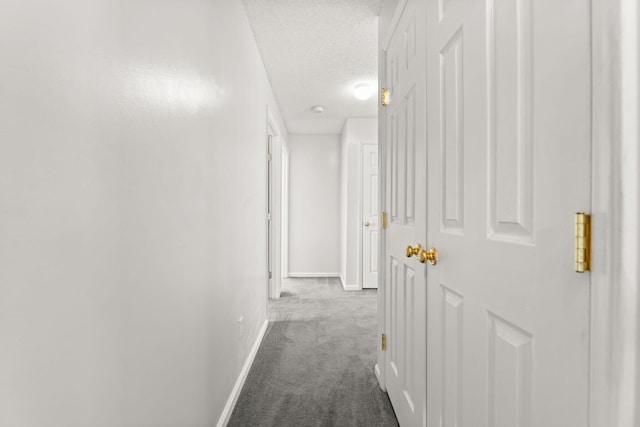 corridor with baseboards, dark colored carpet, and a textured ceiling