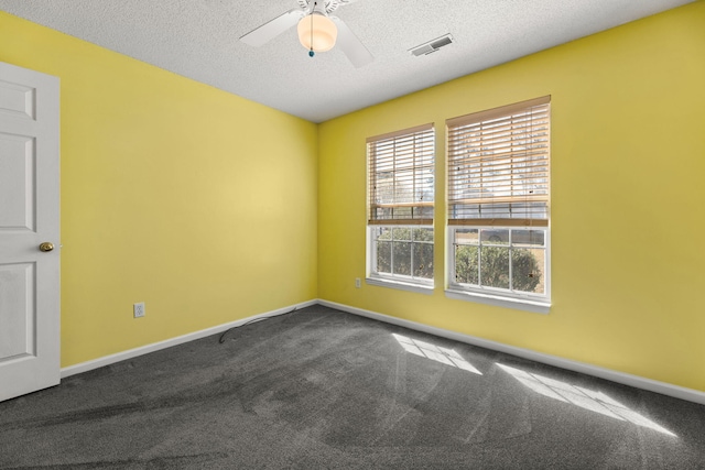 empty room with a textured ceiling, dark colored carpet, visible vents, and baseboards