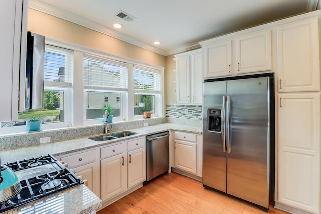 kitchen featuring stainless steel appliances, a sink, white cabinetry, ornamental molding, and light stone countertops