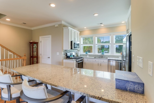 kitchen featuring stainless steel appliances, a breakfast bar, a sink, white cabinetry, and light stone countertops