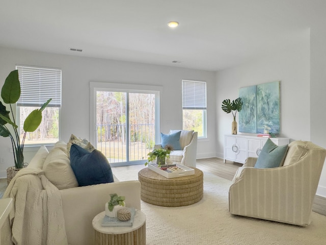 living area with baseboards, wood finished floors, visible vents, and a healthy amount of sunlight