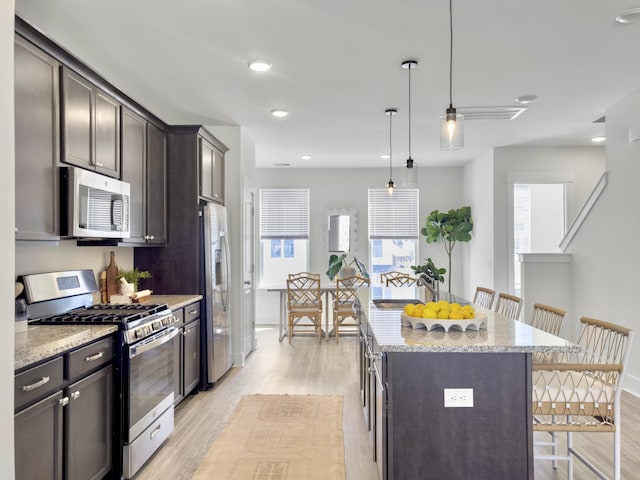 kitchen with light wood-style flooring, a kitchen island, appliances with stainless steel finishes, a breakfast bar area, and light stone countertops