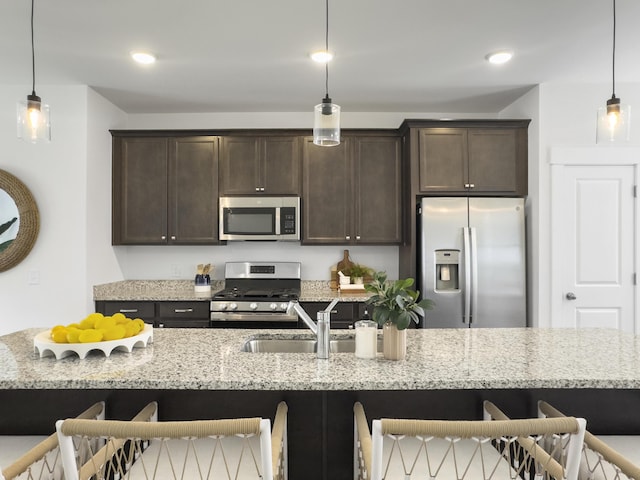 kitchen with pendant lighting, stainless steel appliances, dark brown cabinetry, light stone countertops, and a kitchen breakfast bar