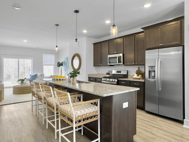 kitchen featuring stainless steel appliances, light wood-type flooring, dark brown cabinets, and a kitchen bar