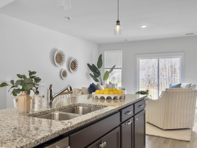 kitchen with visible vents, light wood-style flooring, light stone counters, hanging light fixtures, and a sink