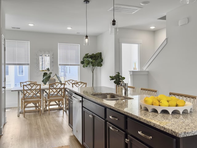 kitchen featuring decorative light fixtures, light wood-style floors, a kitchen island with sink, a sink, and light stone countertops