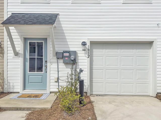 doorway to property with a garage, concrete driveway, and roof with shingles