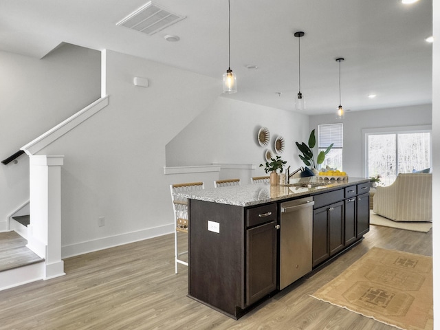 kitchen with light stone counters, visible vents, light wood-style flooring, stainless steel dishwasher, and a sink