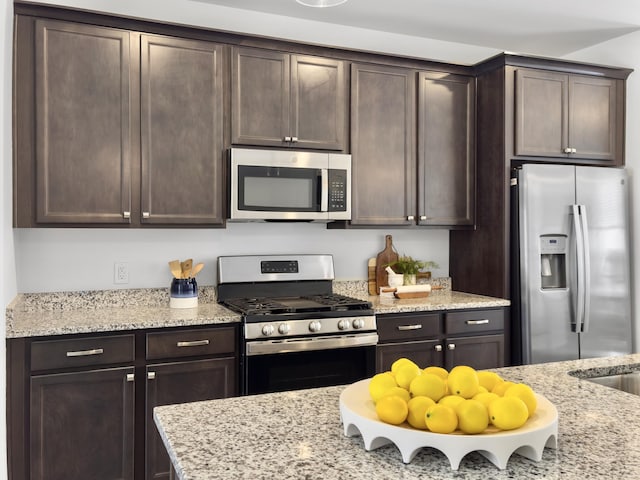 kitchen with stainless steel appliances, light stone counters, and dark brown cabinetry