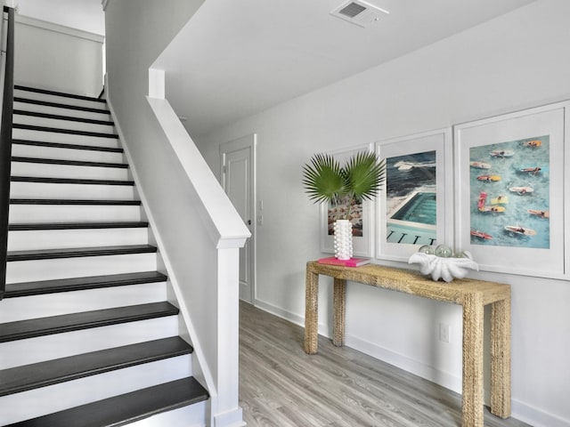 staircase with baseboards, visible vents, and wood finished floors