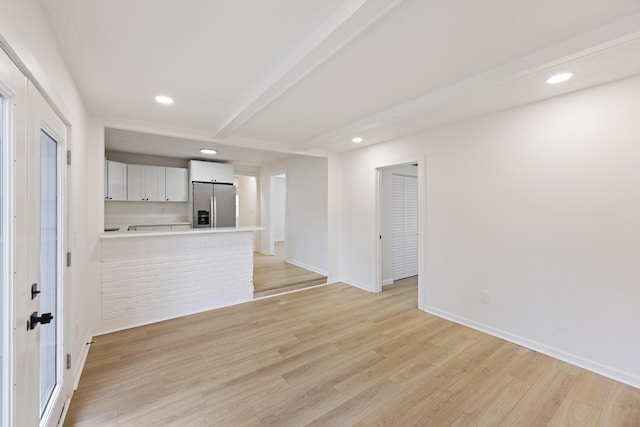 unfurnished living room featuring beamed ceiling and light wood-type flooring