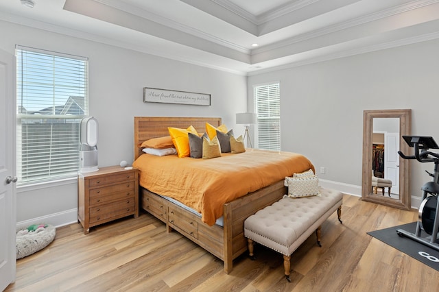 bedroom with ornamental molding, a tray ceiling, and light hardwood / wood-style flooring