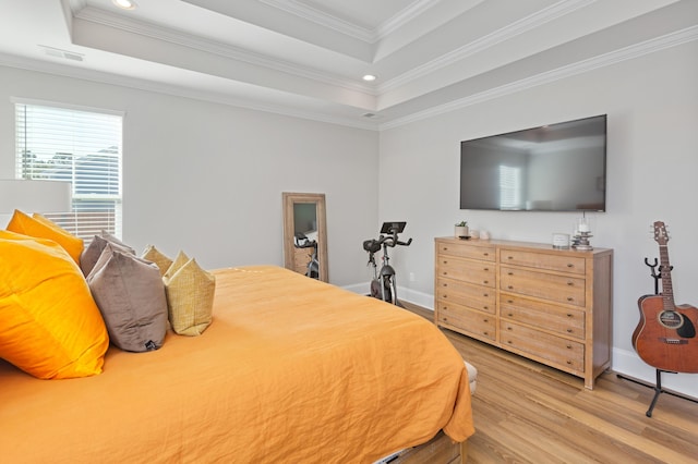 bedroom with ornamental molding, light hardwood / wood-style flooring, and a tray ceiling