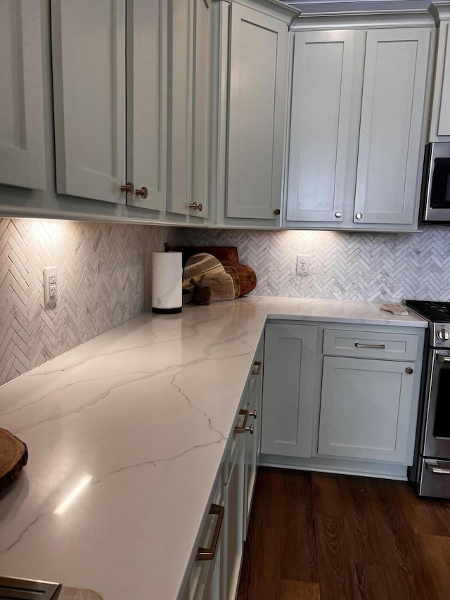 kitchen featuring dark wood-type flooring, stainless steel gas range, light stone counters, gray cabinets, and decorative backsplash