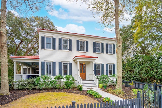 colonial inspired home featuring a ceiling fan, fence private yard, covered porch, and metal roof