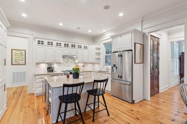 kitchen with a breakfast bar area, backsplash, stainless steel refrigerator with ice dispenser, under cabinet range hood, and visible vents