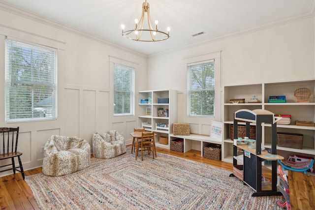 recreation room with wainscoting, an inviting chandelier, wood finished floors, crown molding, and a decorative wall