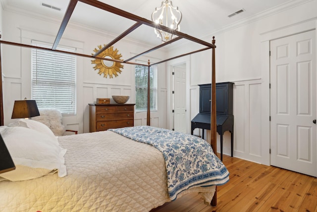bedroom with a decorative wall, a chandelier, visible vents, and hardwood / wood-style floors