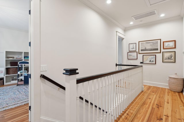 corridor with wood finished floors, visible vents, crown molding, and an upstairs landing