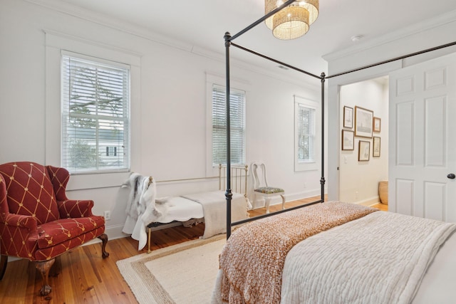 bedroom featuring wood finished floors, crown molding, baseboards, and multiple windows