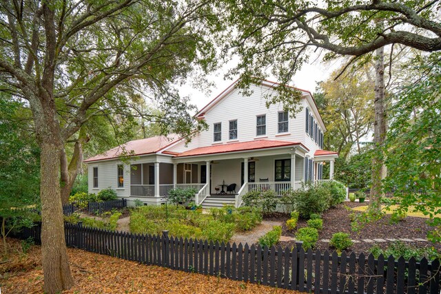 victorian house featuring metal roof, a porch, and a fenced front yard