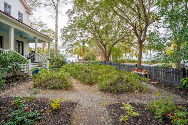 view of yard featuring covered porch, a ceiling fan, stairway, and fence