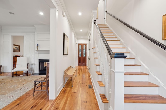 staircase featuring recessed lighting, visible vents, a multi sided fireplace, ornamental molding, and hardwood / wood-style flooring