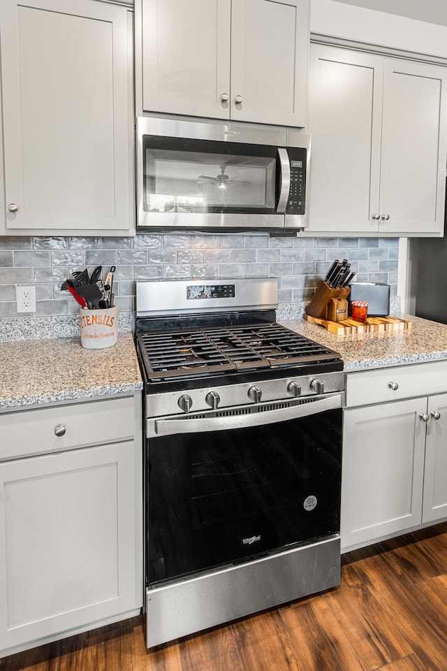 kitchen featuring white cabinets, tasteful backsplash, stainless steel appliances, light stone countertops, and dark hardwood / wood-style flooring