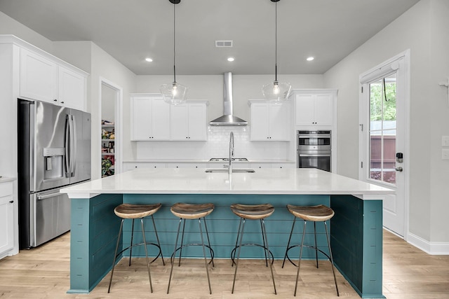 kitchen with stainless steel appliances, wall chimney exhaust hood, light wood finished floors, backsplash, and a large island