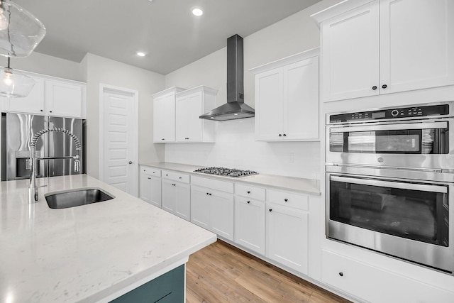 kitchen with wall chimney exhaust hood, stainless steel appliances, light wood finished floors, white cabinetry, and a sink