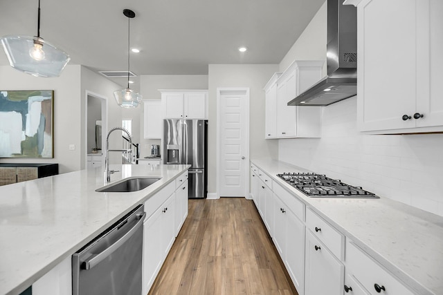 kitchen with wall chimney range hood, a sink, appliances with stainless steel finishes, decorative backsplash, and white cabinetry