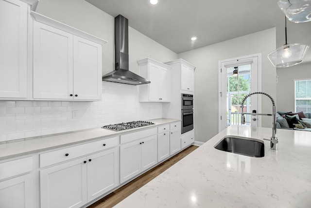 kitchen with wall chimney exhaust hood, a sink, stainless steel appliances, white cabinets, and backsplash