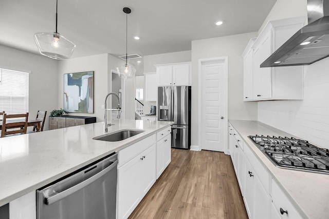 kitchen featuring appliances with stainless steel finishes, a sink, wall chimney range hood, white cabinets, and wood finished floors