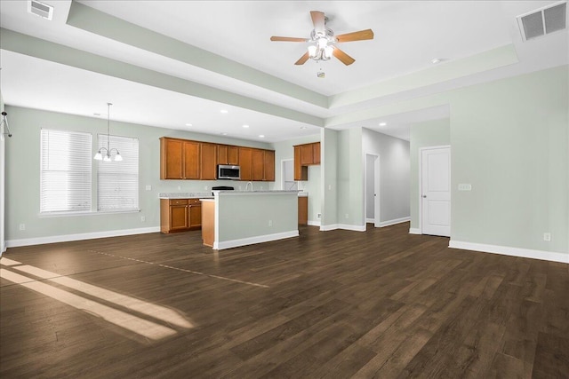 kitchen featuring ceiling fan with notable chandelier, a tray ceiling, dark hardwood / wood-style floors, a kitchen island, and hanging light fixtures