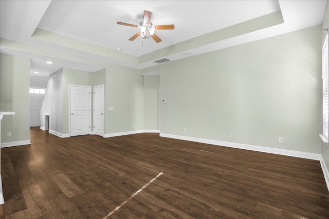 spare room with dark hardwood / wood-style floors, ceiling fan, and a raised ceiling