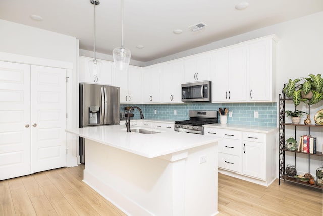 kitchen with an island with sink, stainless steel appliances, white cabinets, and sink