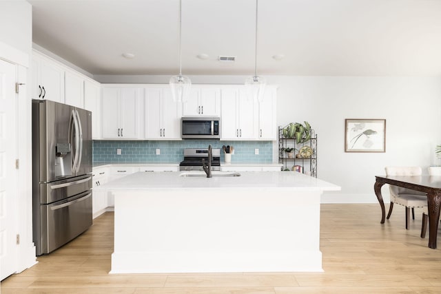 kitchen featuring a kitchen island with sink, pendant lighting, stainless steel appliances, and white cabinets