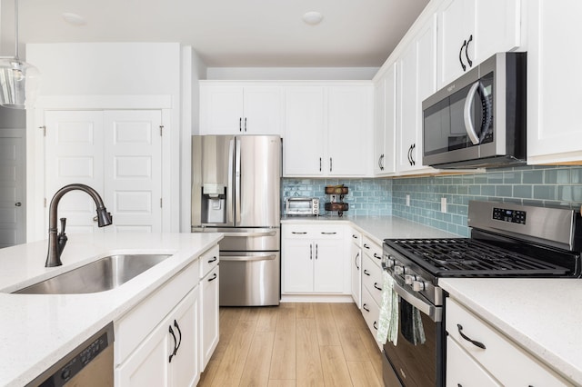 kitchen featuring white cabinetry, pendant lighting, stainless steel appliances, light wood-type flooring, and sink