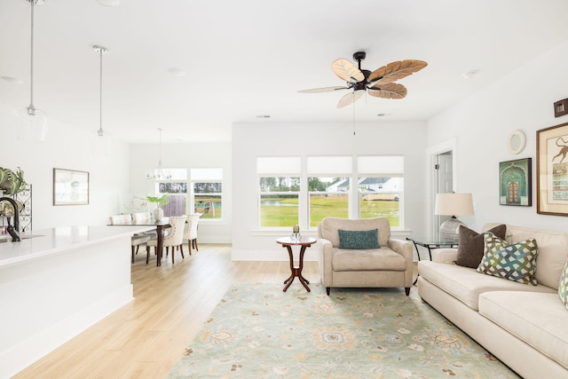 living room featuring ceiling fan with notable chandelier and light wood-type flooring