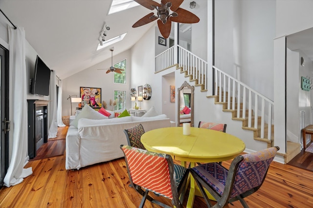 dining area featuring high vaulted ceiling, a skylight, light wood-type flooring, and ceiling fan