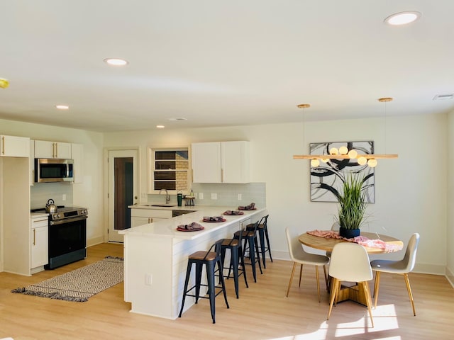 kitchen with electric range oven, tasteful backsplash, sink, decorative light fixtures, and white cabinets