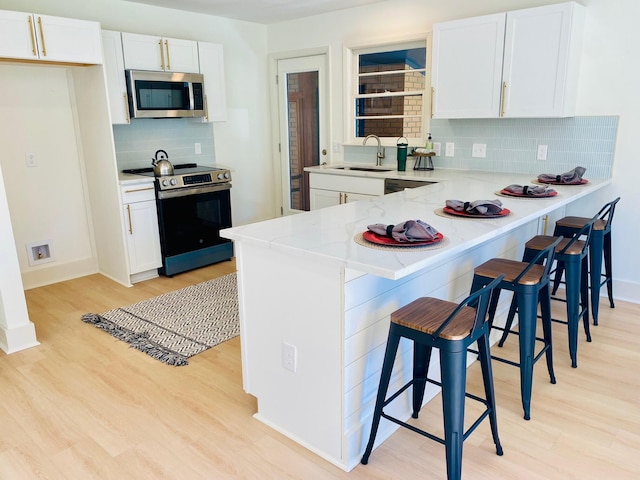 kitchen featuring tasteful backsplash, white cabinetry, stainless steel appliances, and light hardwood / wood-style floors