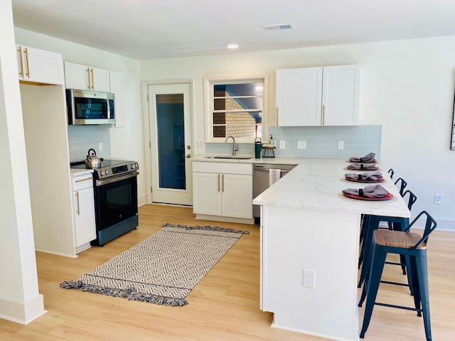 kitchen with appliances with stainless steel finishes, backsplash, sink, light hardwood / wood-style flooring, and white cabinetry