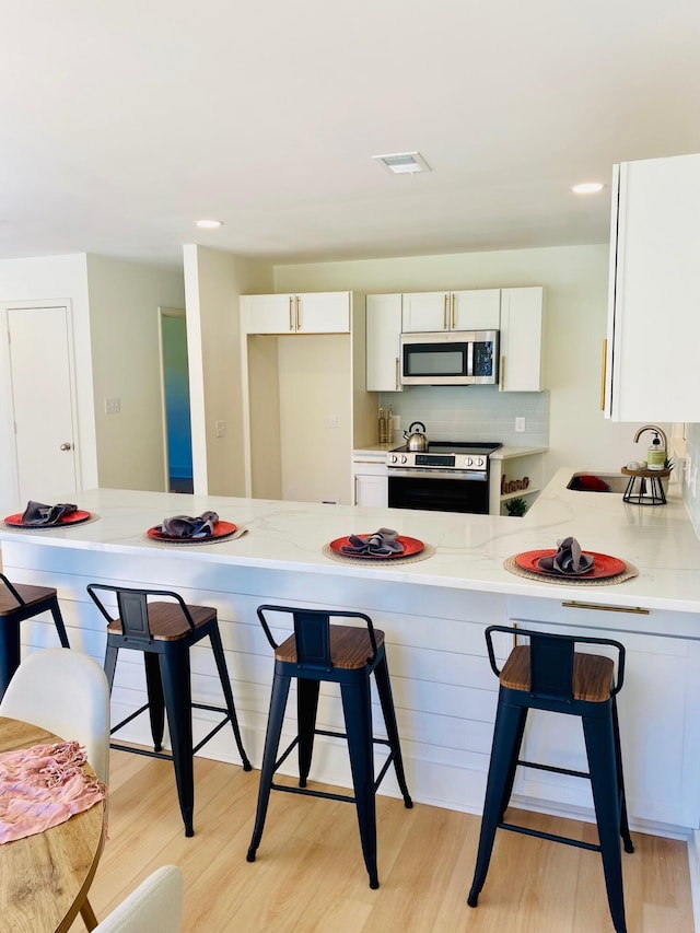 kitchen with a kitchen bar, white cabinetry, and appliances with stainless steel finishes