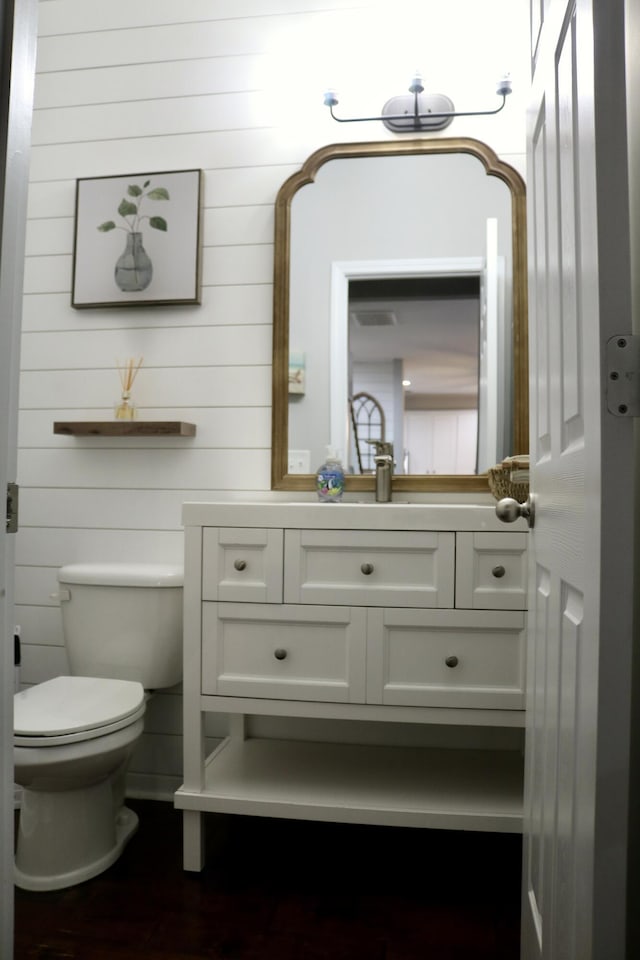 bathroom featuring toilet, wood walls, and vanity