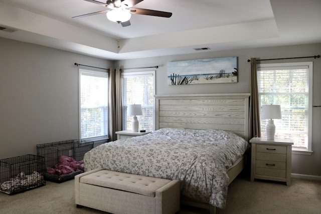 bedroom with ceiling fan, multiple windows, and a raised ceiling