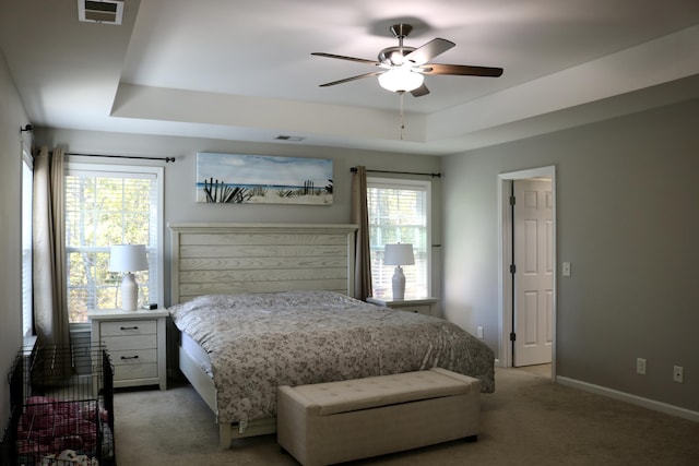 bedroom featuring multiple windows, ceiling fan, a tray ceiling, and carpet